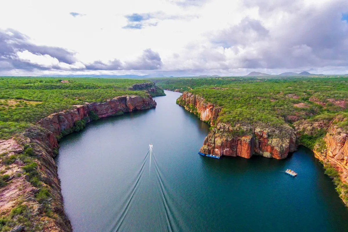 Vista aérea dos cânions de Canindé de São Francisco, com um barco navegando entre as formações rochosas e vegetação ao redor.