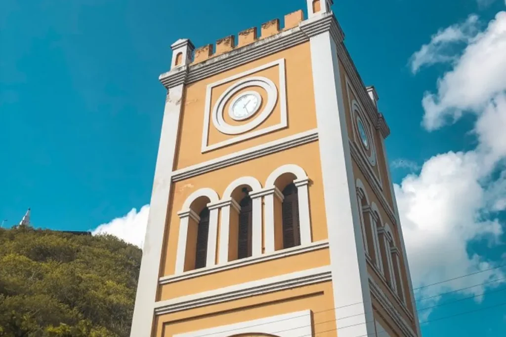 Torre amarela com relógio da Igreja de Santo Antônio de Lisboa sob céu azul claro, com detalhes em branco e estilo arquitetônico clássico