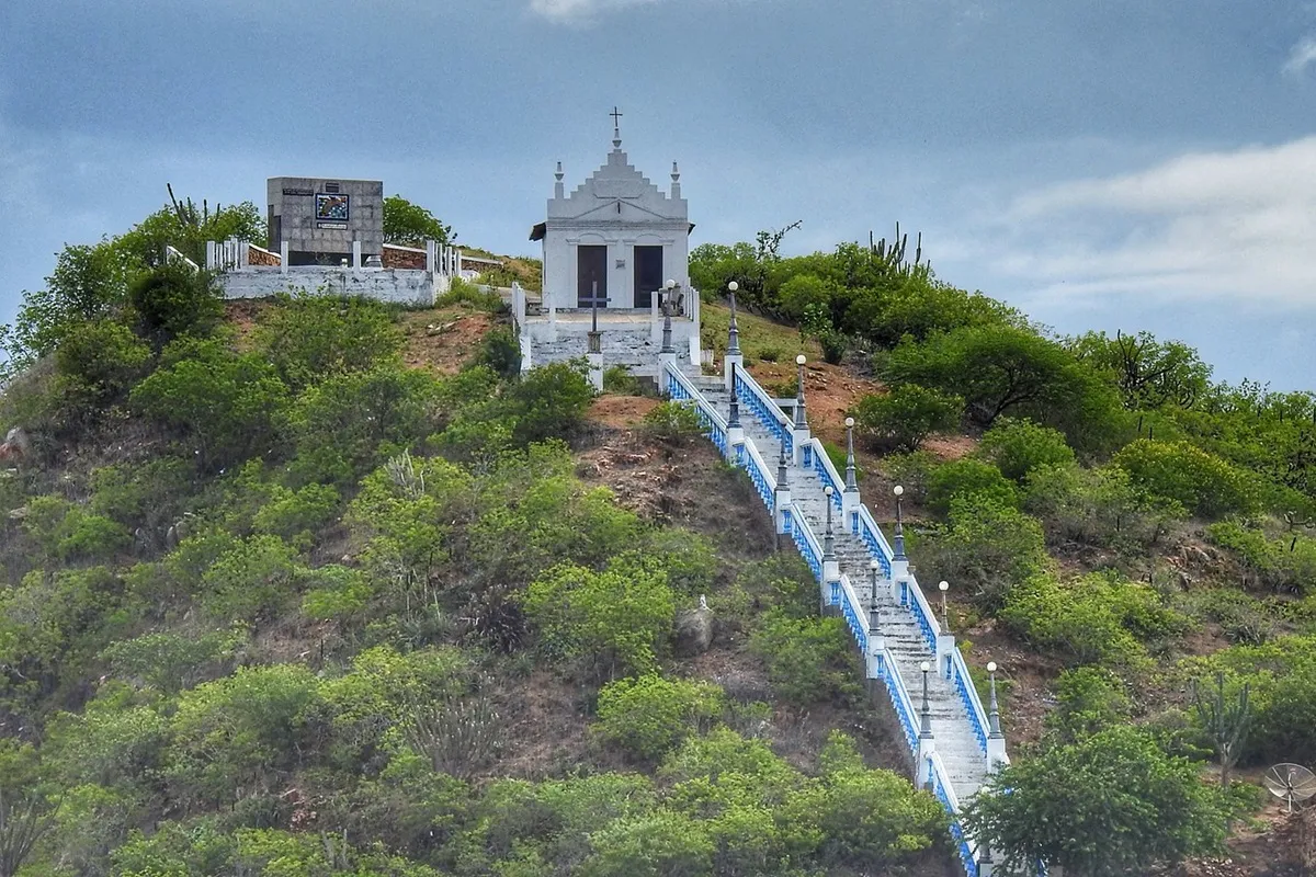 Capela do Bonfim no topo de um morro com uma escadaria azul e branca cercada por vegetação, em ambiente natural e tranquilo.