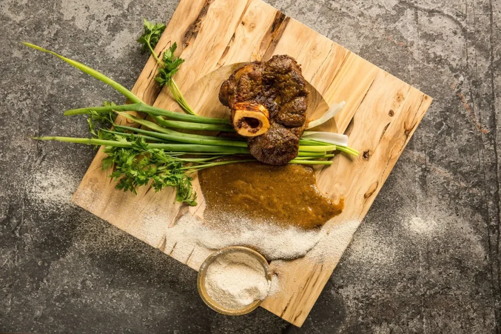 Prato de chambaril com ossobuco e molho, decorado com ervas frescas sobre uma tábua rústica
